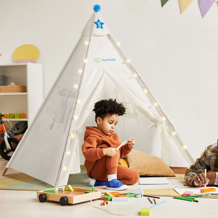 The little boy is sitting in front of a white tent.