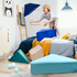 A young boy throws pieces of the Tangram play couch in a bedroom filled with playful decor.