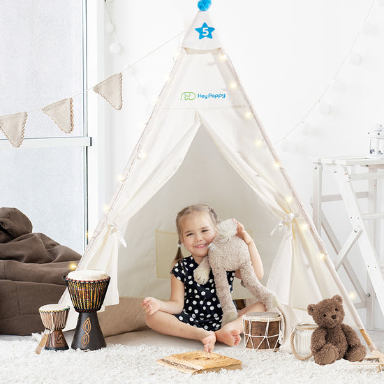 A little girl is sitting inside a white kid's tent with a tambourine, holding a stuffed toy.