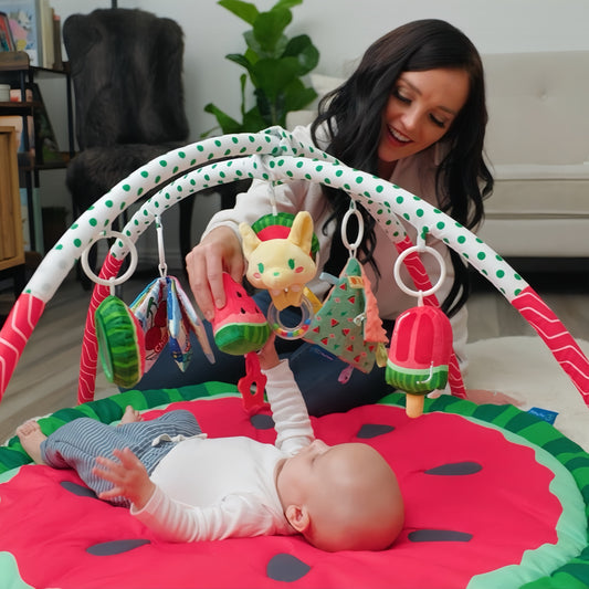 Little baby playing on a watermelon-shaped baby gym with mom's help