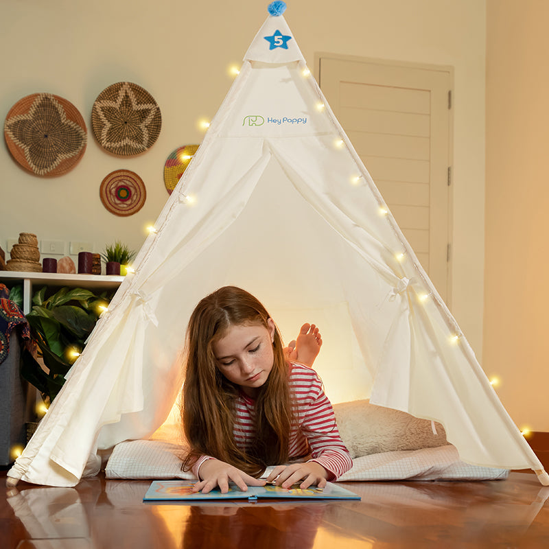 A little girl is reading a storybook inside a white kid's tent.